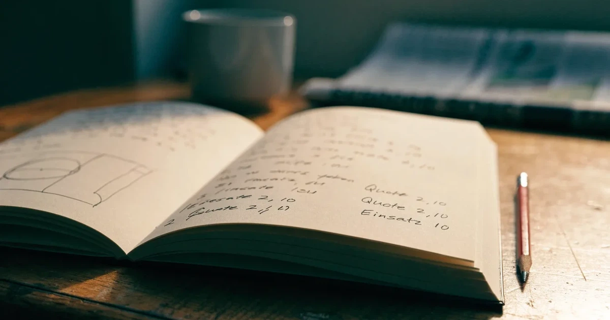 Ein Notizbuch mit handschriftlichen Notizen und kleinen Skizzen liegt aufgeschlagen neben einem Bleistift auf einem Schreibtisch, Fensterlicht von links.